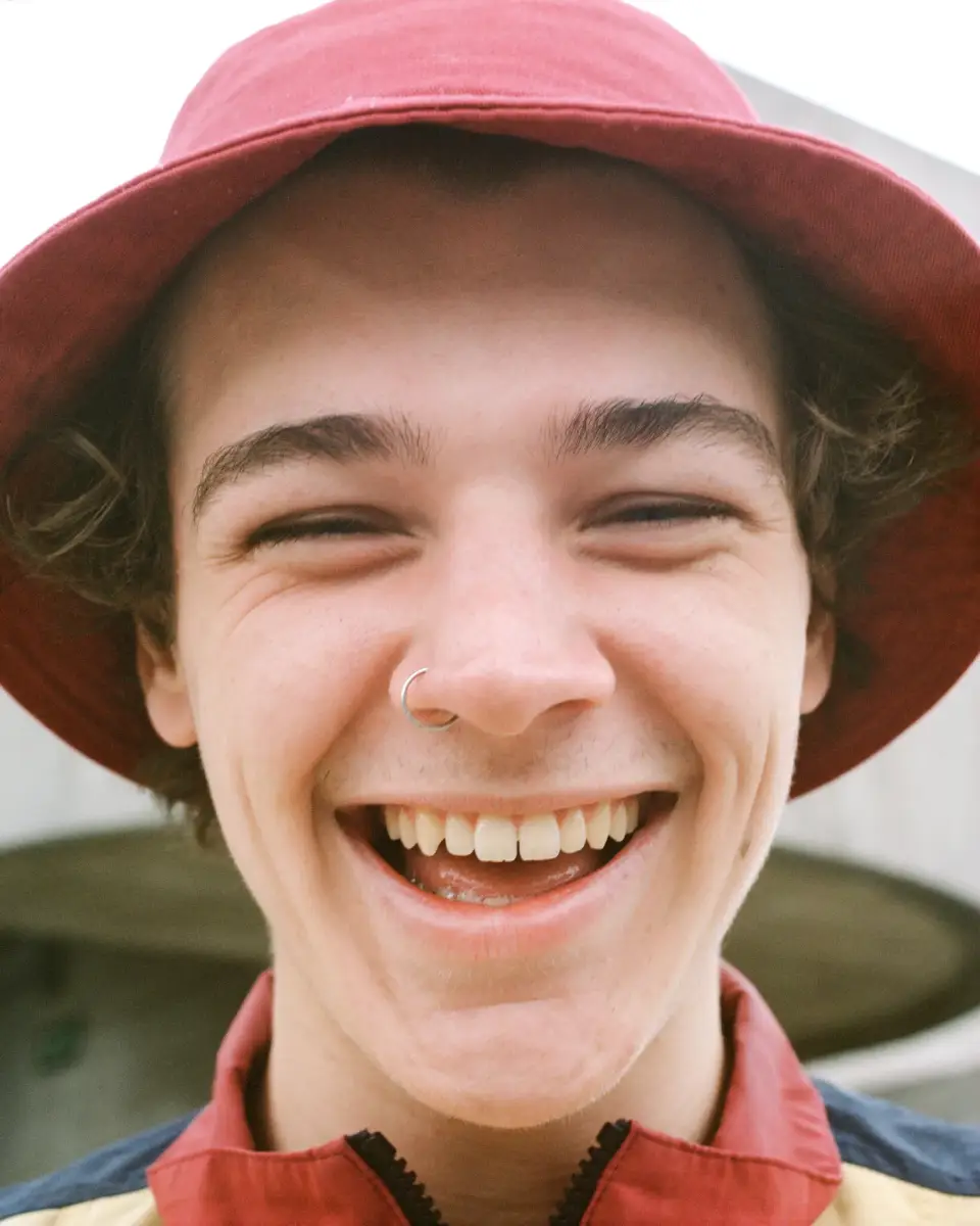 Een close-up portret van een lachende, jongen man die een rode bucket hat draagt