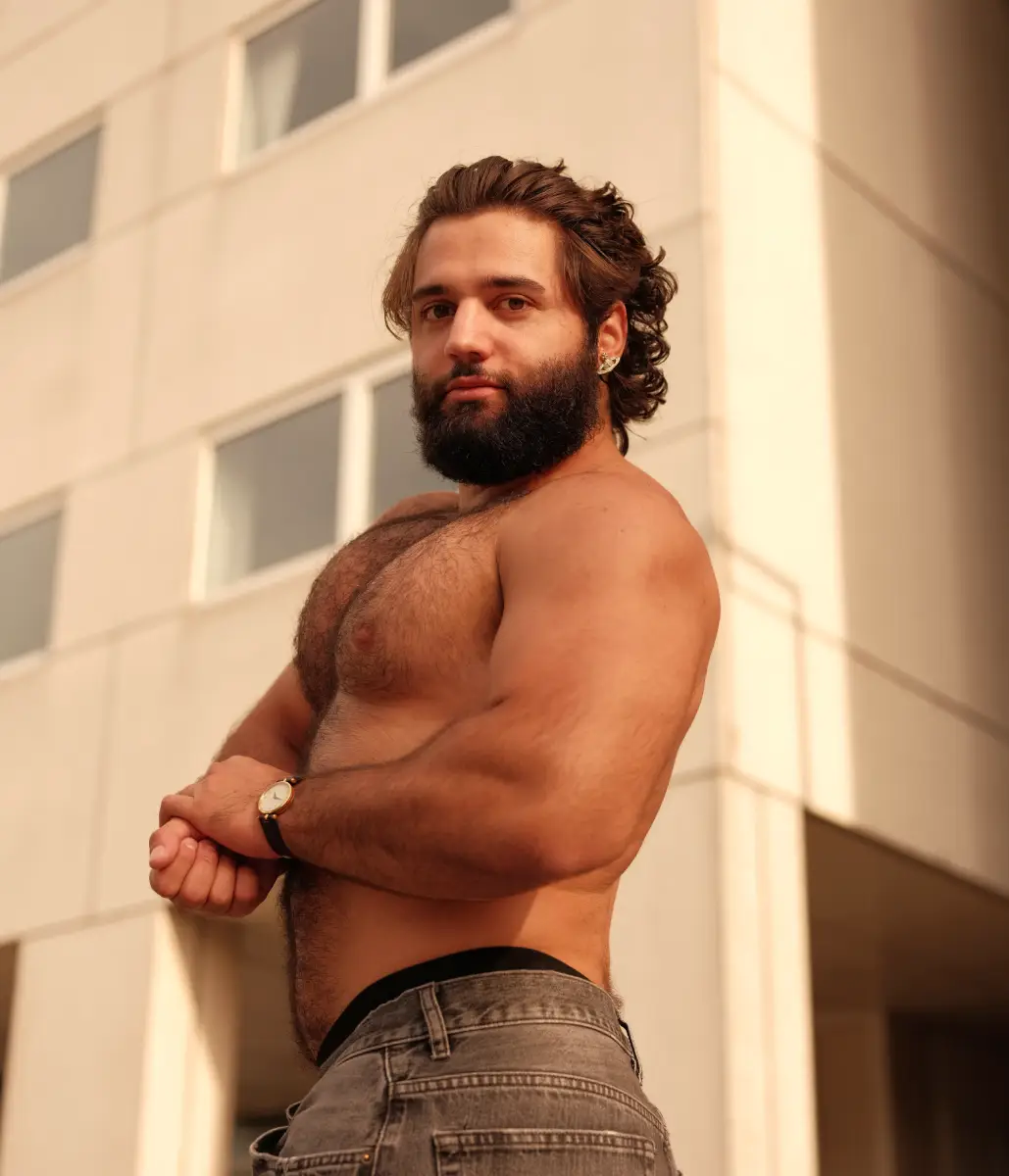 Een portret van een shirtless man die zijn spieren laat zien in een industriele omgeving.