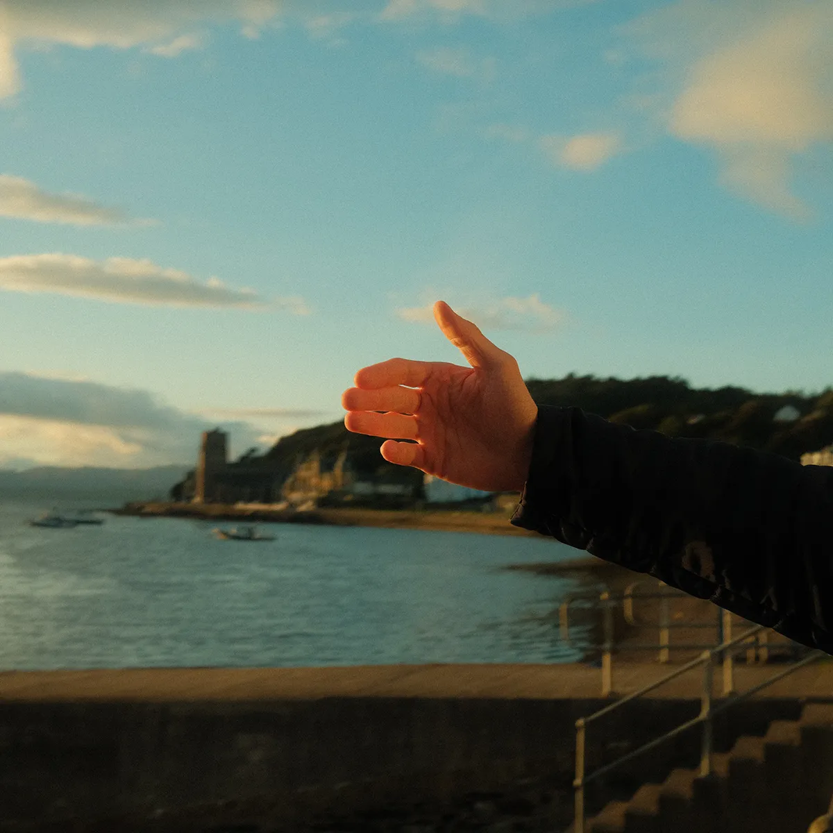 Een foto van een hand die meet waar de horizon is, we bekijken de hand vanaf de zijkant en zien het licht tussen de vingers door een oranje gloed geven.