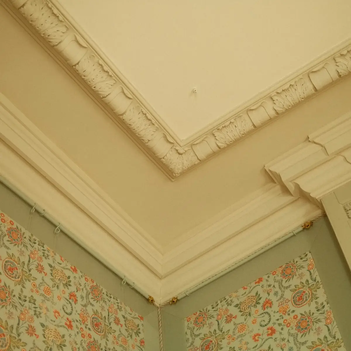 Ornamenten op een plafond gefotografeerd in de hoek van een kamer met een jaren 50 behang
